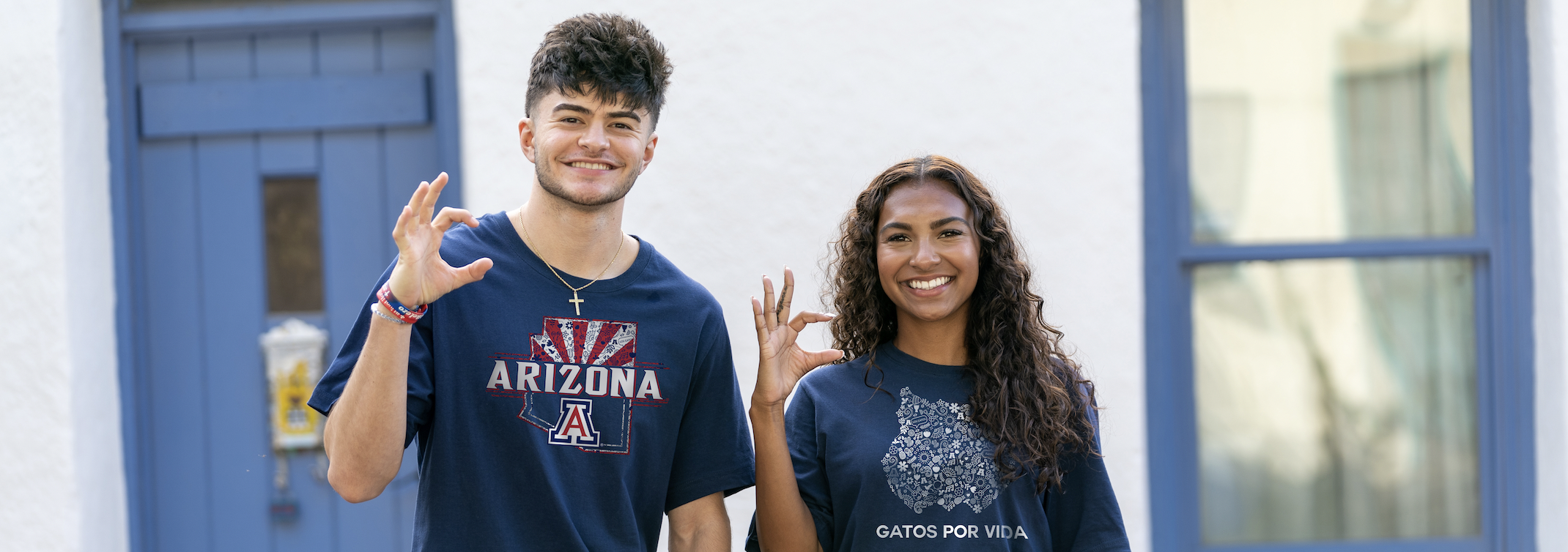 A boy and girl student in University of Arizona t-shirts holding up the Wildcats hand sign.